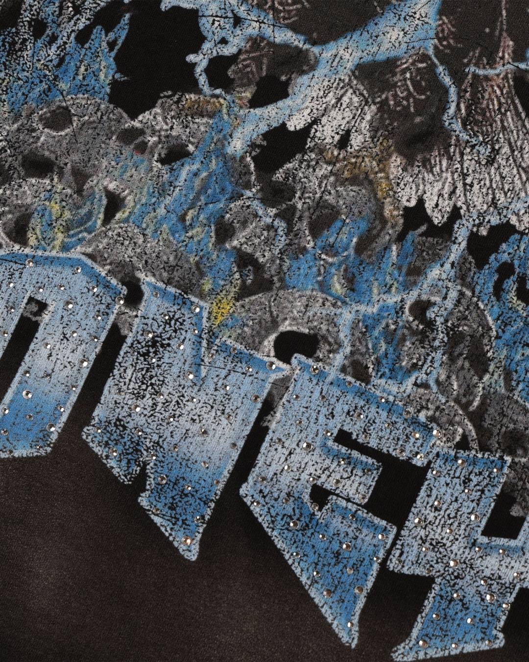 Close-up of a graphic print featuring distressed blue and silver lettering over a dark background with abstract black, gray, and blue splatter-like artwork.