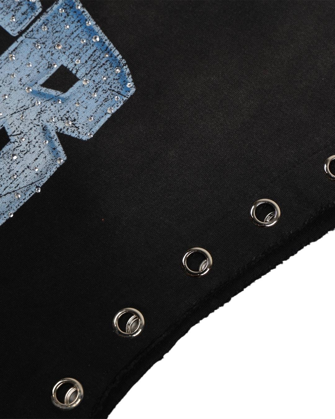Close-up detail of a black garment featuring a distressed light blue graphic letter and silver metal grommets along the edge, set against a white background.