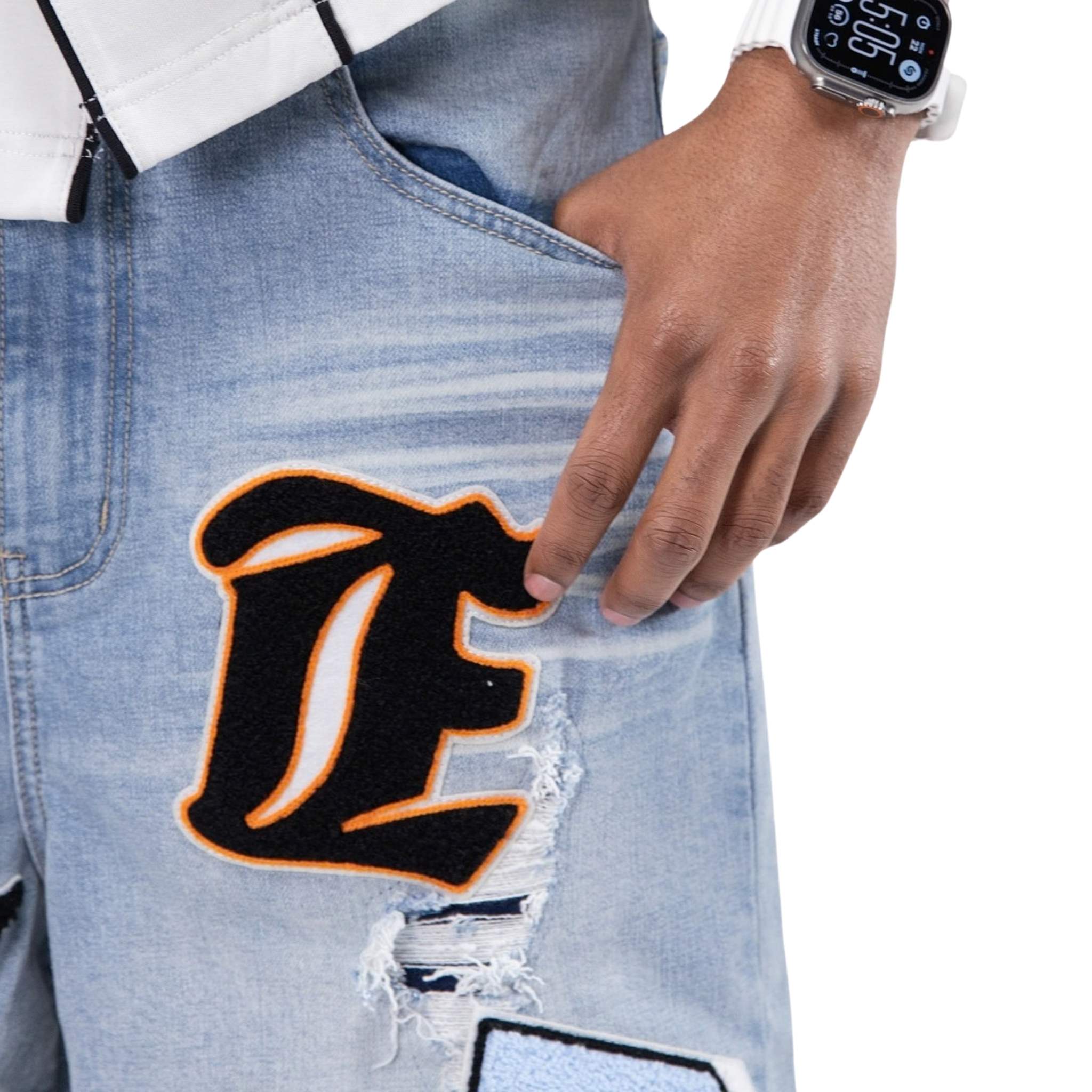 Close-up of a person wearing ripped jeans with a large letter 'E' patch, holding a phone.